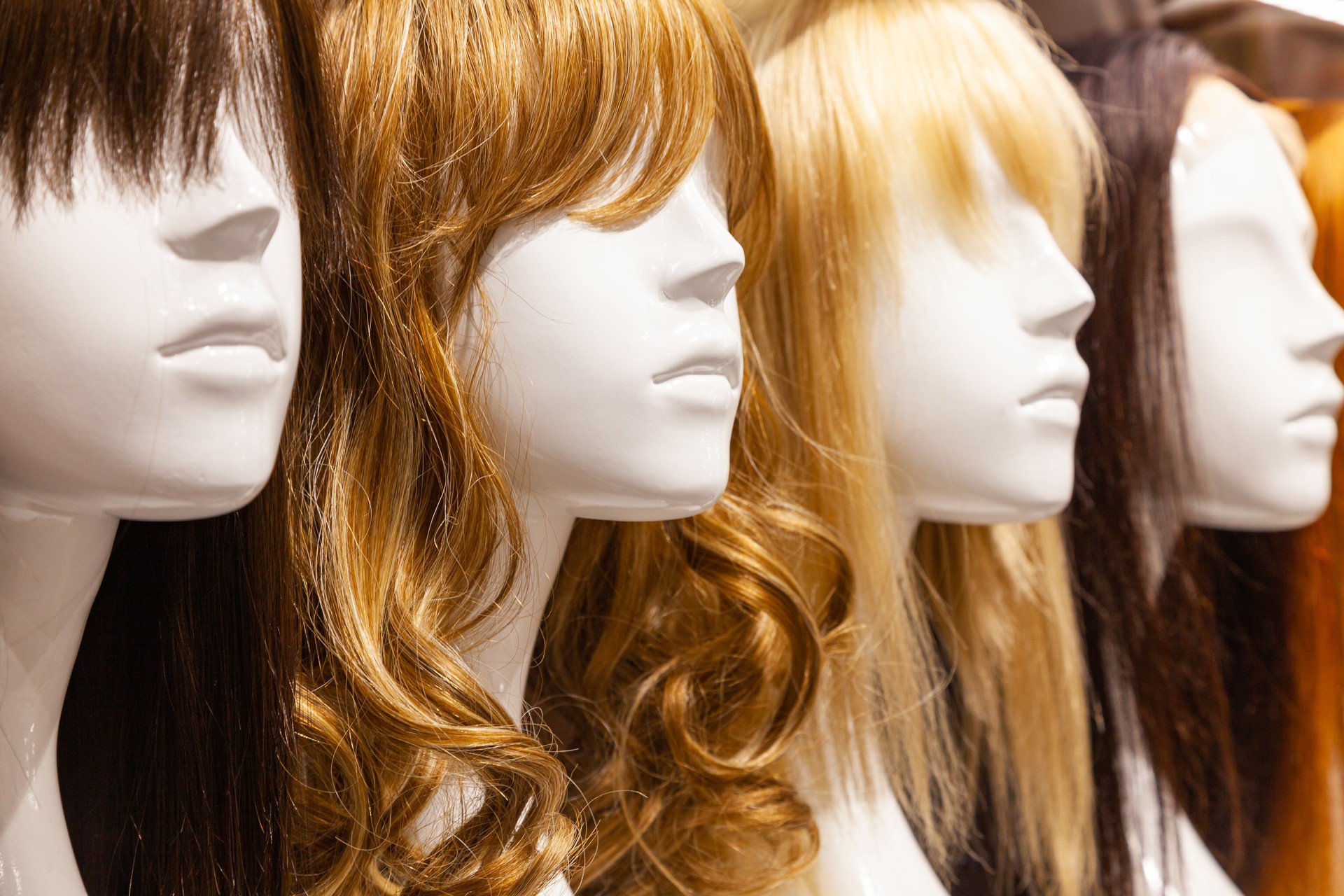 Multi-colored wigs are worn on the heads of mannequins.